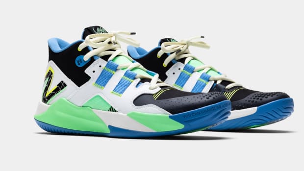 Side view of white, black, and green New Balance tennis shoes.